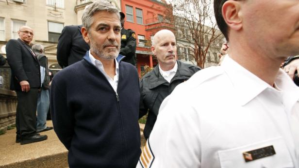 George Clooney steht im Freien, umgeben von anderen Personen.