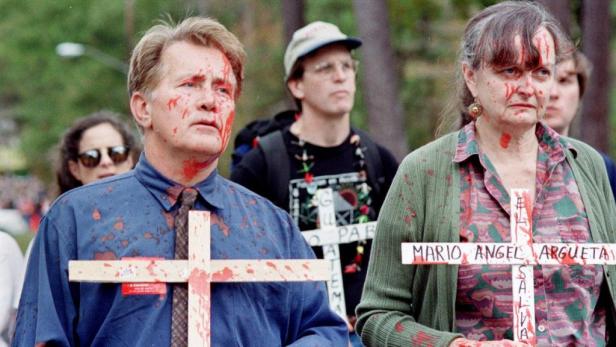 Martin Sheen und eine Frau mit blutbefleckter Kleidung und Kreuzen bei einer Demonstration.