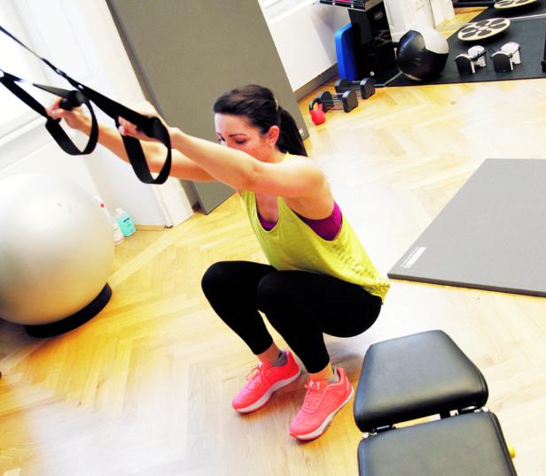 Health PI Stoffwechsel-Messung, Bodyblog… Eine Frau macht Kniebeugen mit einem Schlingentrainer in einem Fitnessstudio.