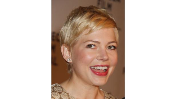 Michelle Williams lächelt mit kurzem blonden Haar und roten Lippen.