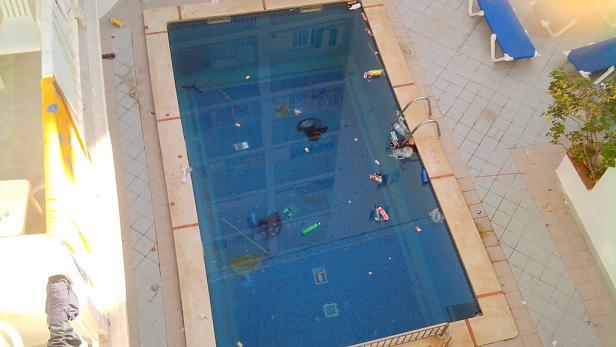 Ein verschmutzter Swimmingpool mit Müll und Unrat im Wasser.