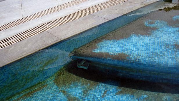 Ein teilweise entleerter Pool mit blauem Mosaik und etwas Schmutz am Boden.