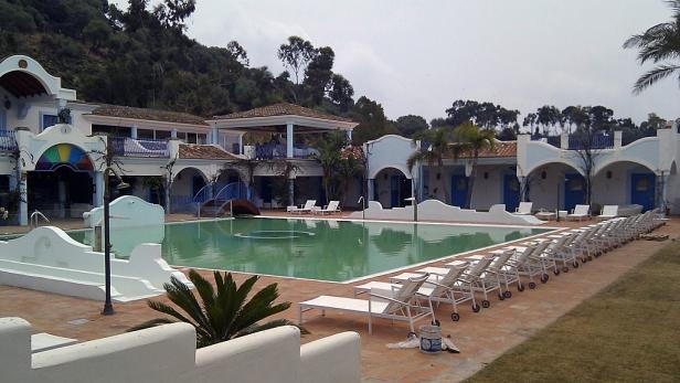 Ein Schwimmbad mit Liegestühlen vor einem Hotel im mediterranen Stil.