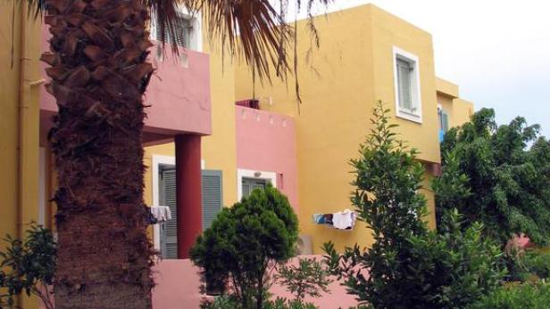 Ein gelbes und rosa Gebäude mit einem Palmenstamm im Vordergrund.