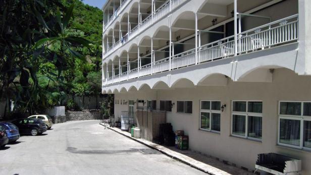 Ein weißes Hotelgebäude mit mehreren Balkonen und geparkten Autos davor.