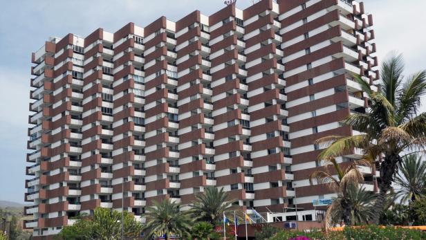 Ein großes, mehrstöckiges Gebäude mit vielen Balkonen und Palmen im Vordergrund.