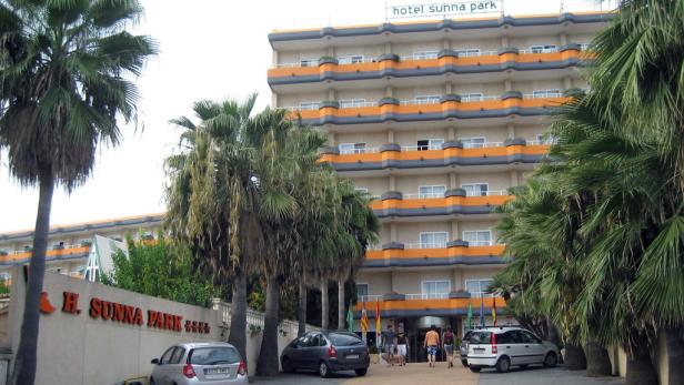 Das Hotel Sunna Park mit Palmen und parkenden Autos vor dem Eingang.