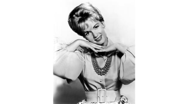 Eine lächelnde Frau mit Halskette und hochgesteckten Haaren posiert.