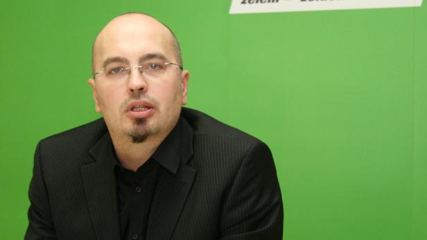 Ein Mann mit Brille und Bart vor einem grünen Hintergrund.