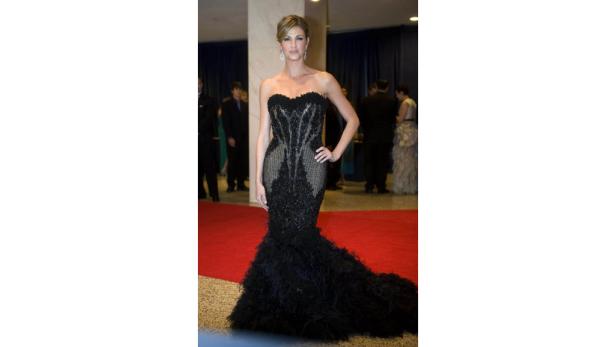 Eine Frau in einem schwarzen, trägerlosen Abendkleid mit Federn posiert auf einem roten Teppich.