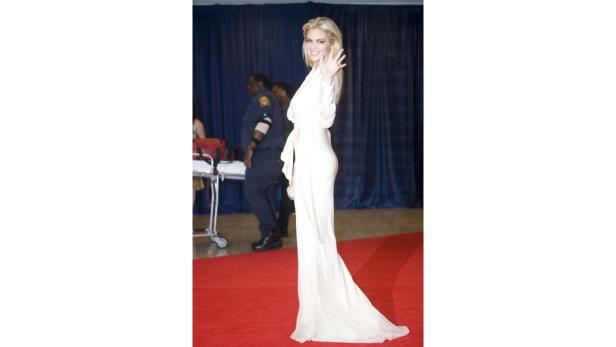 Eine Frau in einem weißen Kleid winkt auf einem roten Teppich.