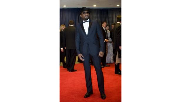 Ein Mann mit Hut und Fliege posiert auf einem roten Teppich.