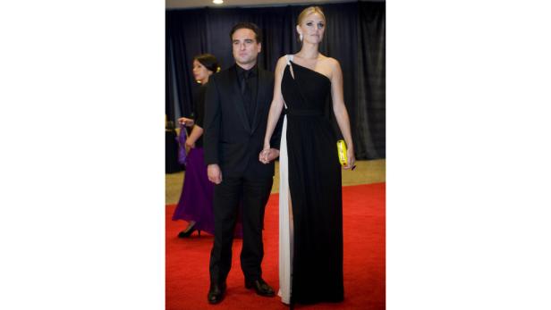 Johnny Galecki und eine Frau in Abendgarderobe halten Händchen auf einem roten Teppich.