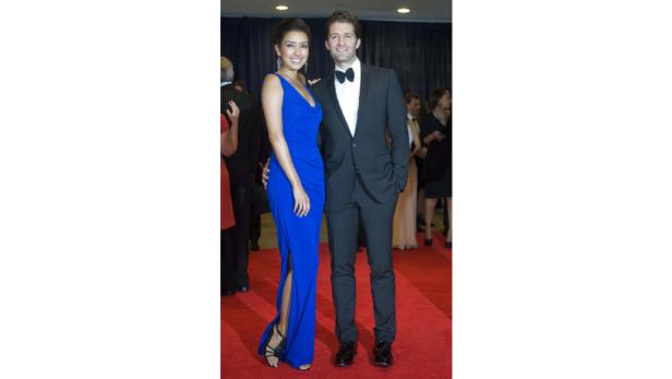 Ein Mann im Anzug und eine Frau im blauen Abendkleid posieren auf einem roten Teppich.