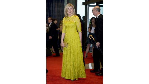 Eine Frau in einem gelben Spitzenkleid auf einem roten Teppich.