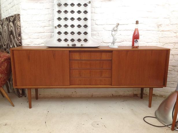Ein Sideboard aus Holz mit einer Flasche Wein und einer Statue darauf vor einer weißen Ziegelwand.