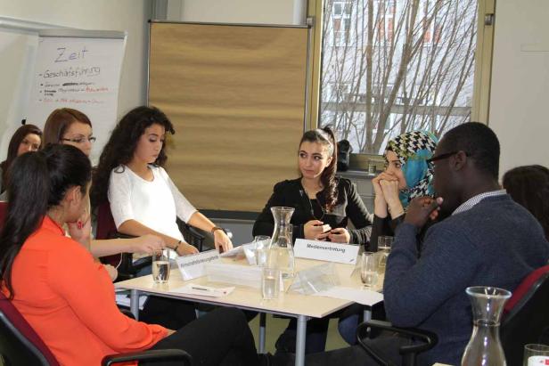 Eine Gruppe junger Erwachsener sitzt an einem Tisch bei einer Besprechung.