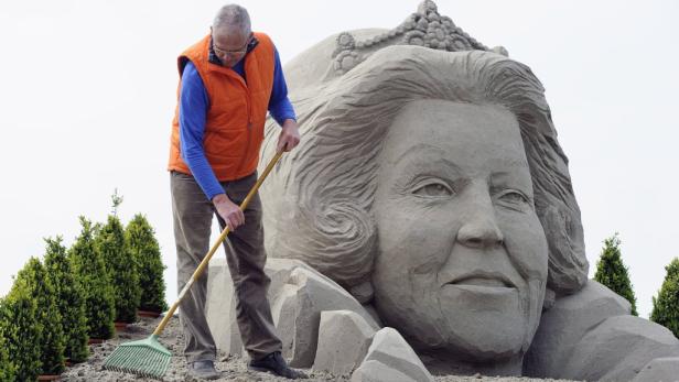 Ein Mann kehrt Sand vor einer großen Sandskulptur, die Königin Beatrix darstellt.