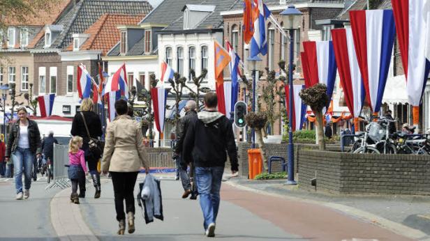 Menschen gehen an einem mit niederländischen Flaggen geschmückten Platz entlang.