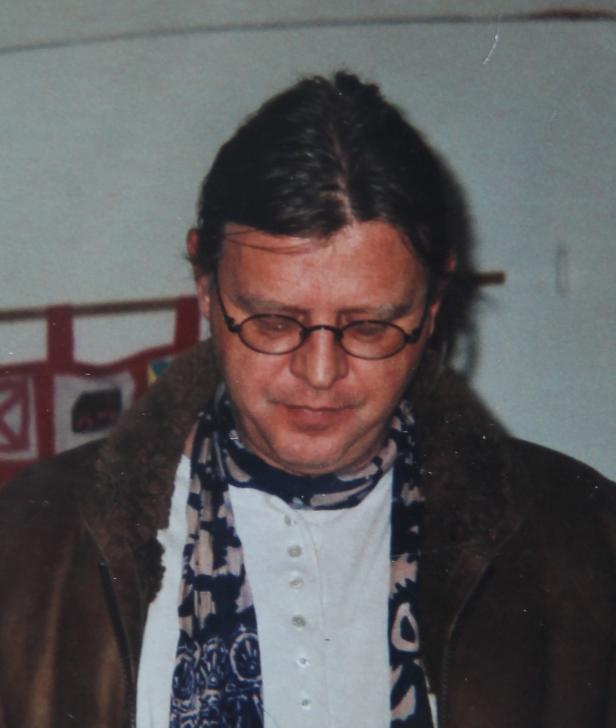 Ein Mann mit Brille, Schal und brauner Jacke blickt nach unten.