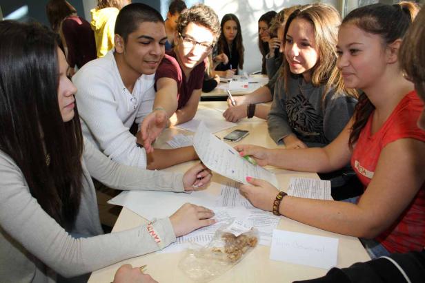 Eine Gruppe junger Leute sitzt an einem Tisch und diskutiert über Dokumente.