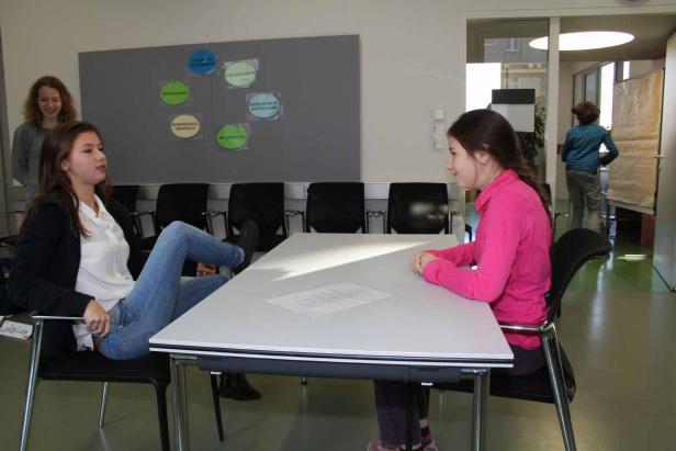 Zwei junge Frauen sitzen an einem Tisch und unterhalten sich.