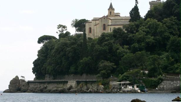 Eine Kirche thront auf einem bewaldeten Hügel an der Küste.