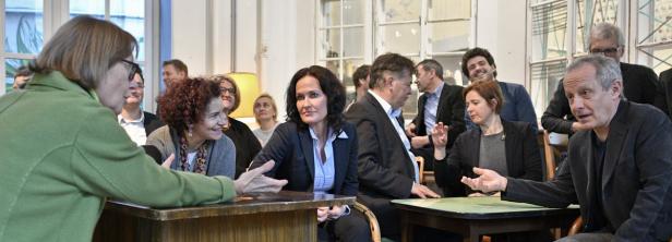 Eine Gruppe von Menschen sitzt an Tischen und diskutiert in einem hellen Raum.