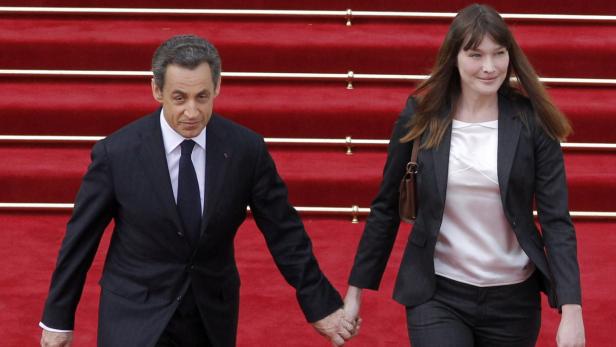 Nicolas Sarkozy und Carla Bruni gehen Händchen haltend eine rote Treppe hinunter.