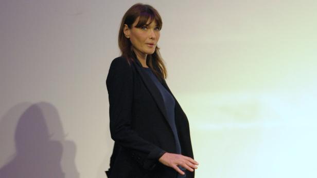 Carla Bruni trägt einen dunklen Blazer vor einem hellen Hintergrund.