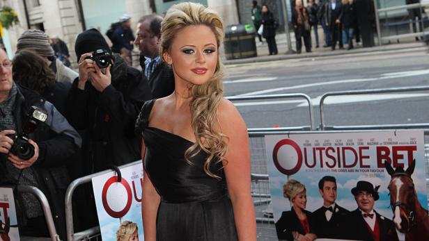 Eine Frau in einem schwarzen Kleid posiert vor dem Filmplakat „Outside Bet“.