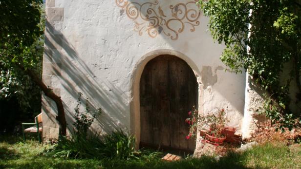 Eine Holztür in einer weiß getünchten Mauer mit floralen Verzierungen.