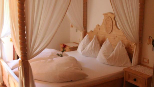 Ein Himmelbett mit weißen Vorhängen und einer einzelnen roten Rose auf dem Kissen.