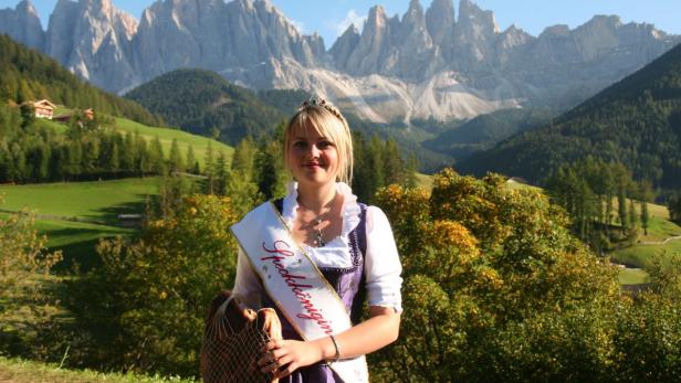 Eine junge Frau, die „Speckkönigin“, trägt ein Dirndl vor einer Bergkulisse.