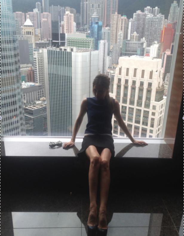 Eine Frau sitzt vor einem Fenster mit Blick auf eine Stadtlandschaft.