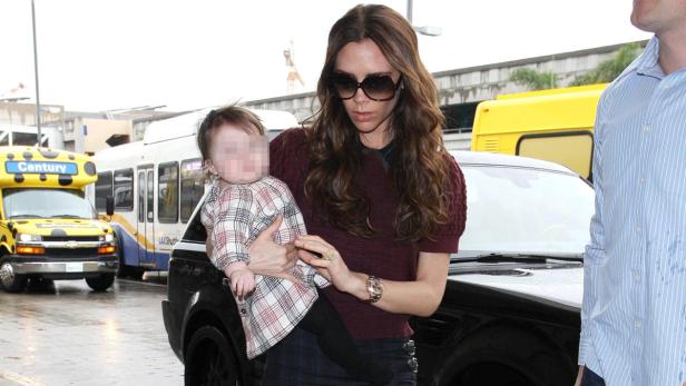 Victoria Beckham trägt ihr Kind auf dem Arm vor einem schwarzen Auto.