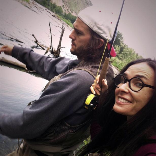 Ashton Kutcher und eine Frau beim Fliegenfischen an einem Fluss.