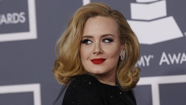 Adele mit roten Lippen und blonden Locken vor einer Grammy-Awards-Wand.