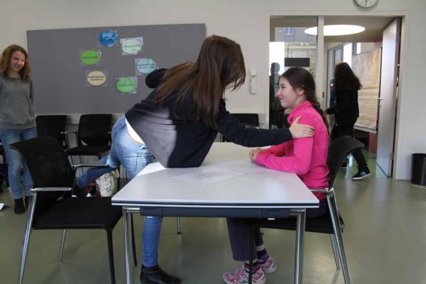 Eine junge Frau tröstet eine andere, die an einem Tisch sitzt.