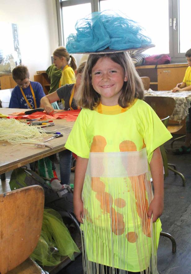 Ein Mädchen mit einem Kostüm und einem blauen Hut auf dem Kopf lächelt.