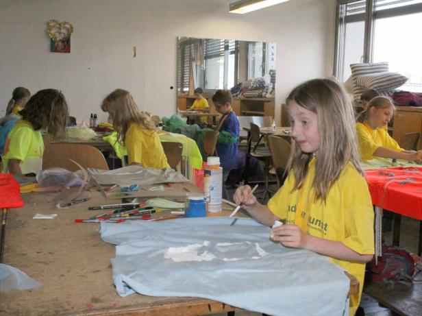 Kinder bemalen in einem Klassenraum T-Shirts mit Farbe.