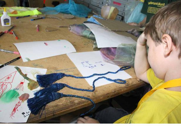 Ein Junge sitzt an einem Tisch mit Bastelmaterialien und Zeichnungen.
