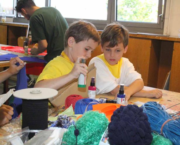 Zwei Jungen sitzen an einem Tisch und basteln mit Sprühfarben und Wolle.