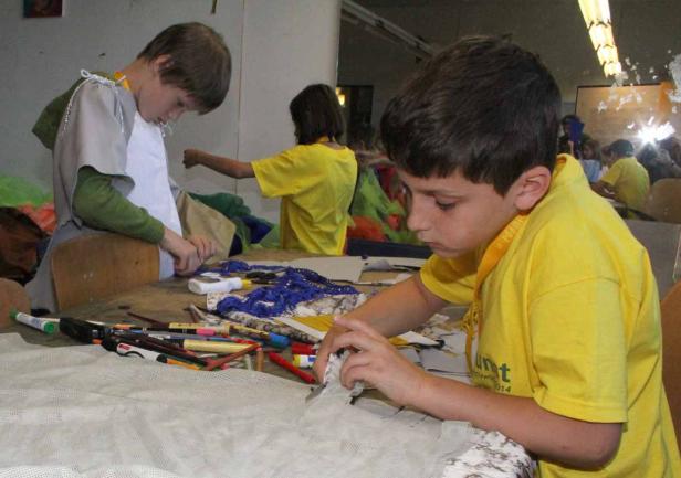 Kinder basteln an einem Tisch mit Stiften und Stoffresten.