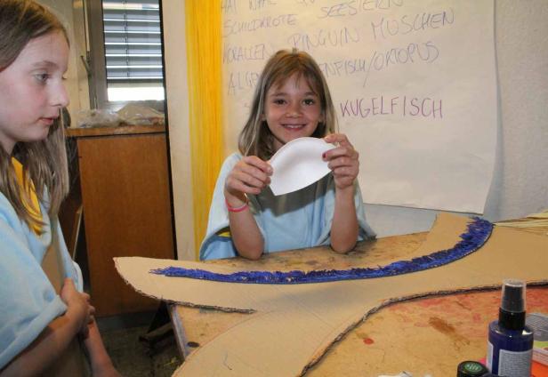 Ein Mädchen bastelt an einem Fischkostüm mit einer Pappmaché-Flosse.