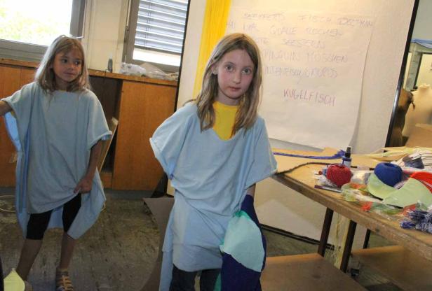 Zwei Mädchen tragen Kostüme in einem Klassenzimmer mit einer Liste von Meerestieren an der Wand.