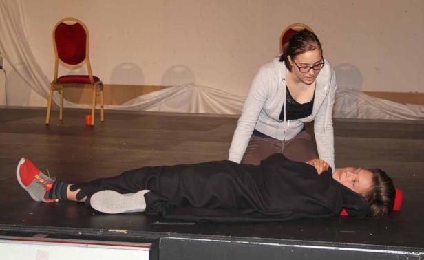 Eine junge Frau kniet neben einer anderen Person, die auf einer Bühne liegt.