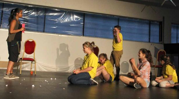 Eine Gruppe junger Leute probt ein Theaterstück auf einer Bühne.