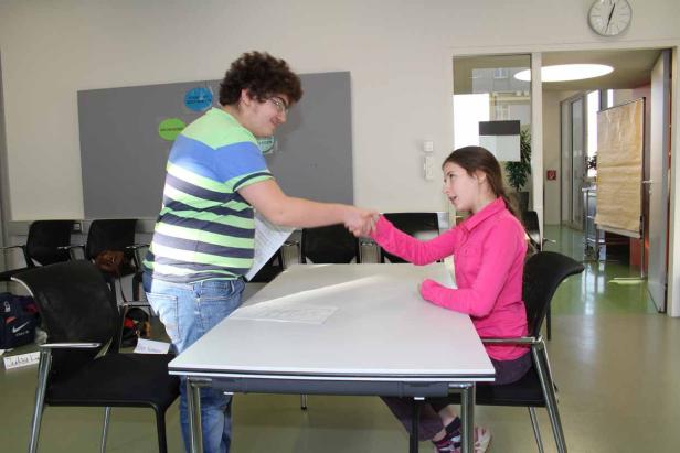 Ein junger Mann und ein junges Mädchen geben sich in einem hellen Raum die Hand.