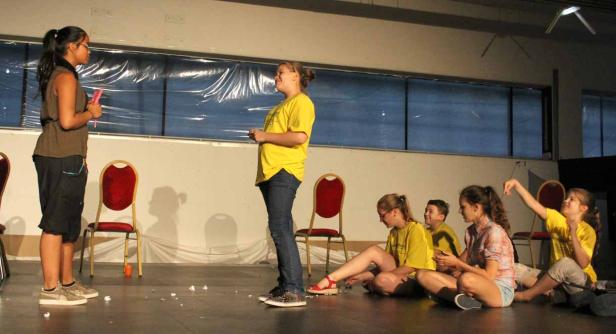 Zwei Mädchen stehen auf einer Bühne, während andere im Publikum sitzen.